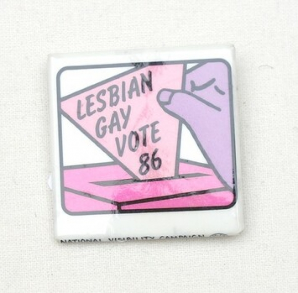 Square badge with a purple hand holding a pink triangle with the text: "LESBIAN GAY VOTE 86". USA, 1986.