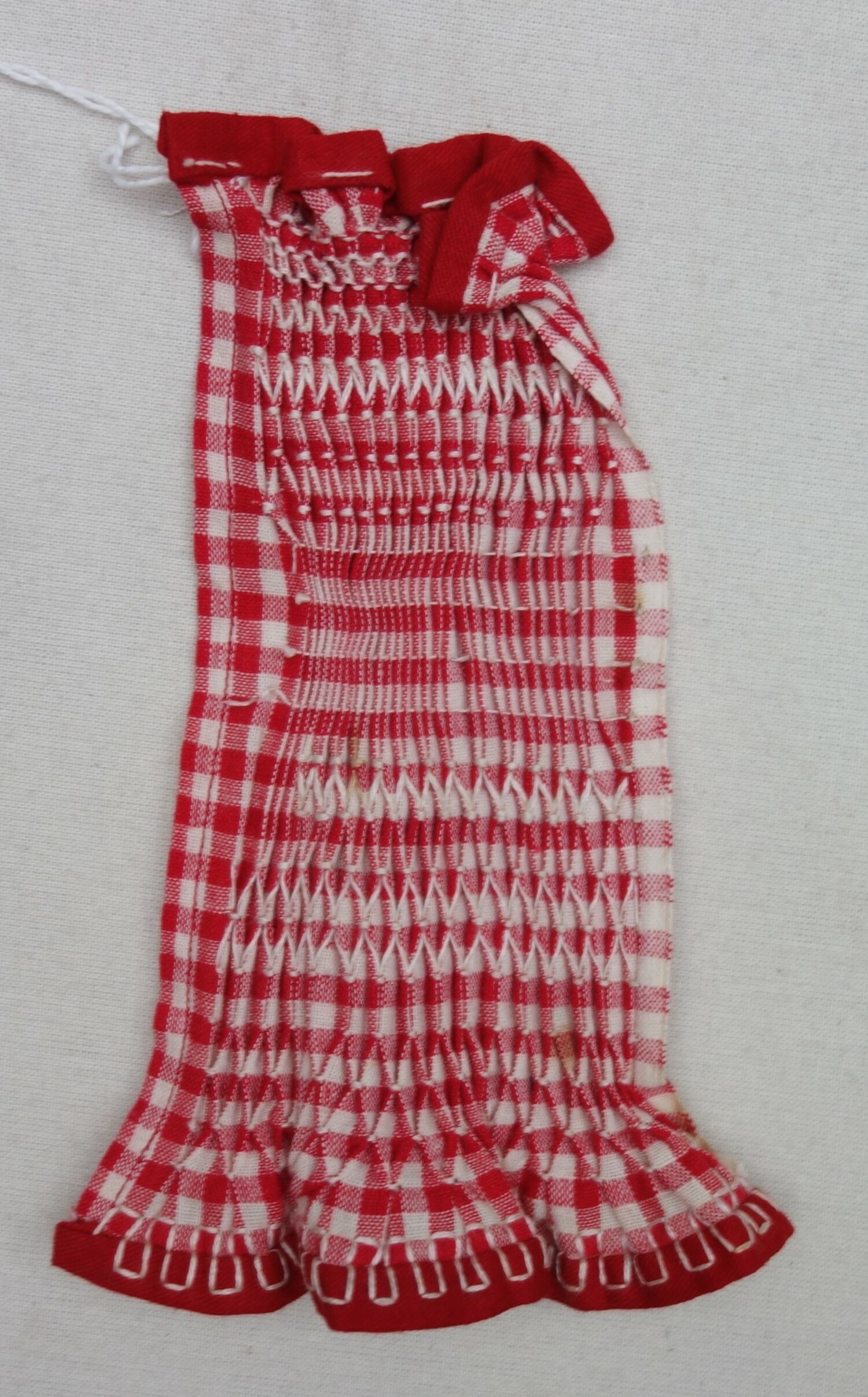 School sample of smocking using a red and white gingham cloth and white embroidery thread. There are over seven different types of decorative effects and stitching. The Netherlands, 20th century (TRC 2023.1516).