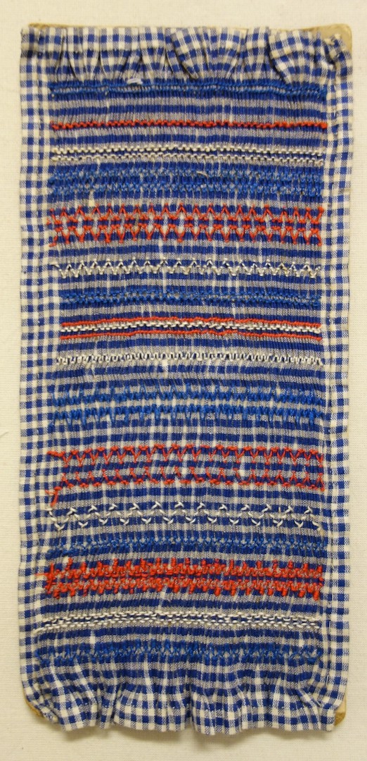 Sample of smocking using a blue and white gingham ground and embroidered in various smocking stitches using white and red yarns. The Netherlands, 20th century (TRC 2024.0165).
