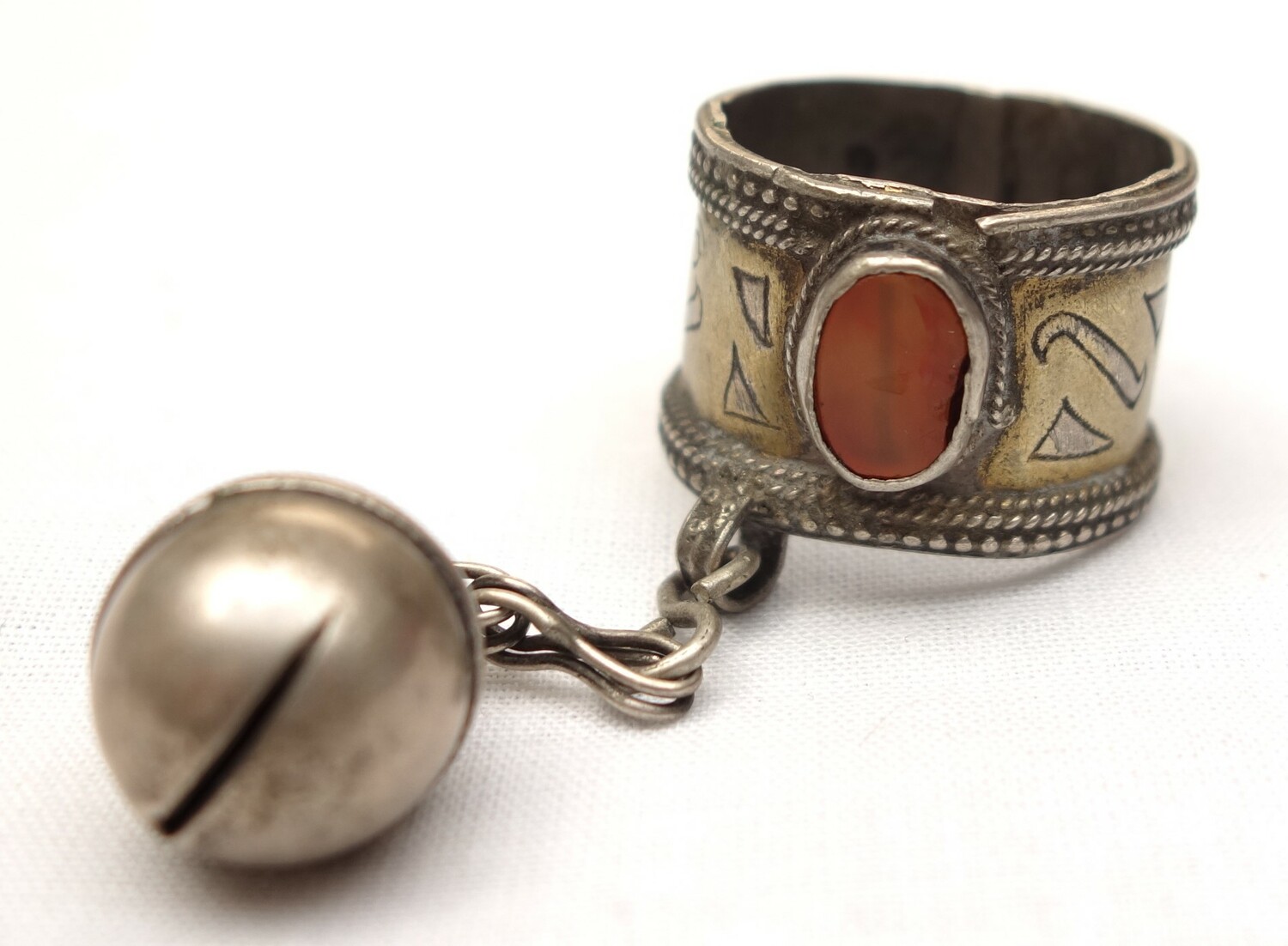 Silver ring with a wide gilded band with granulated borders, an oval orange stone, and a chain with a bell pendant. Afghanistan, 20th century (TRC 2024.0782).