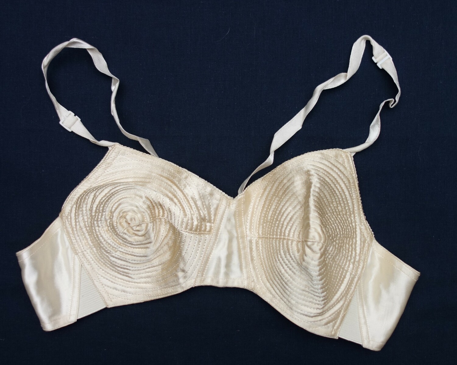 Bra with a small cup size made from a white satin material with foam and elastic fittings. 1940s-1950s (TRC 2024.1182).