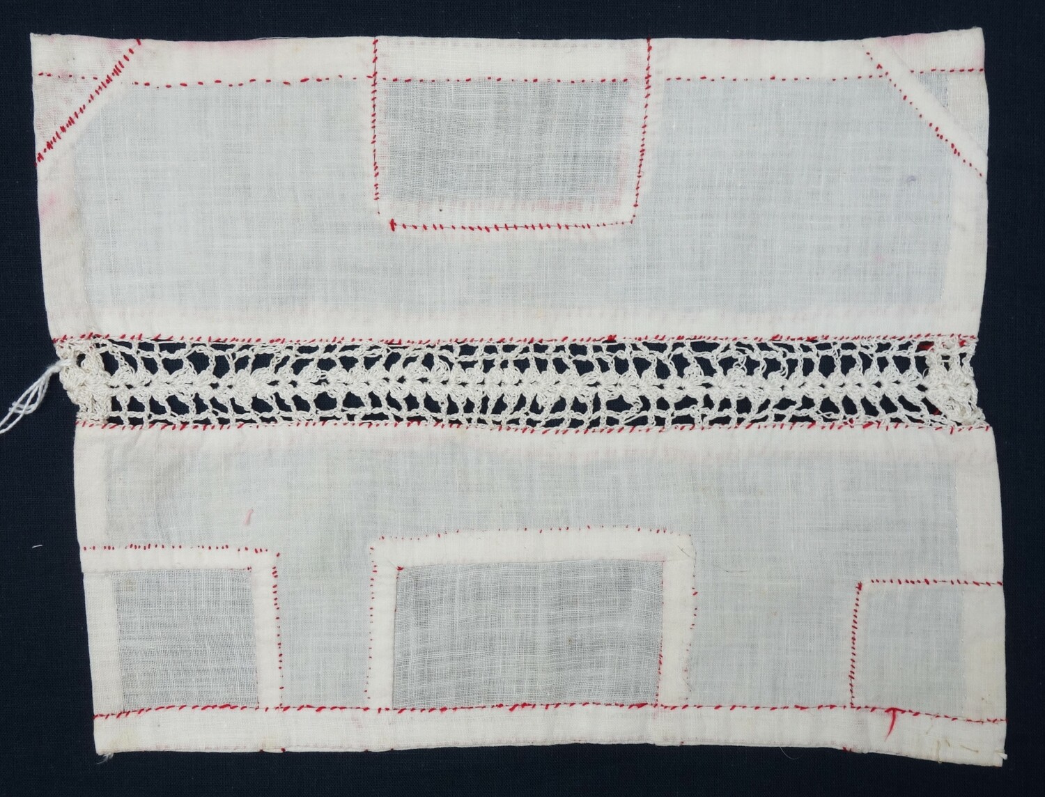 Fig. 1: School sample, worked by a young girl, with six types of patching, stitched with red yarn, and with a crochet inset (insertion) down the middle of the cloth. The Netherlands, early 20th century (TRC 2024.1633).