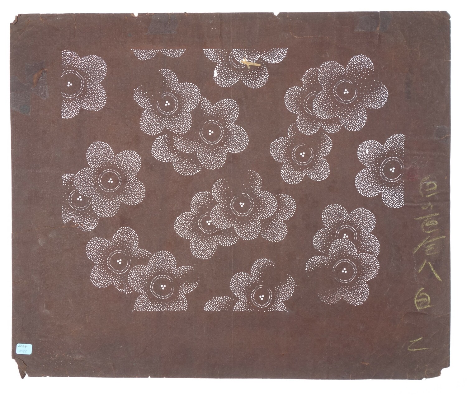 Stencil of mulberry paper, with a pattern of groups of two and three, large stylised flower heads, all worked on tiny dots. There is a hand-written text in Japanese down one side of the stencil. Japan, 20th century (TRC 2024.2033).