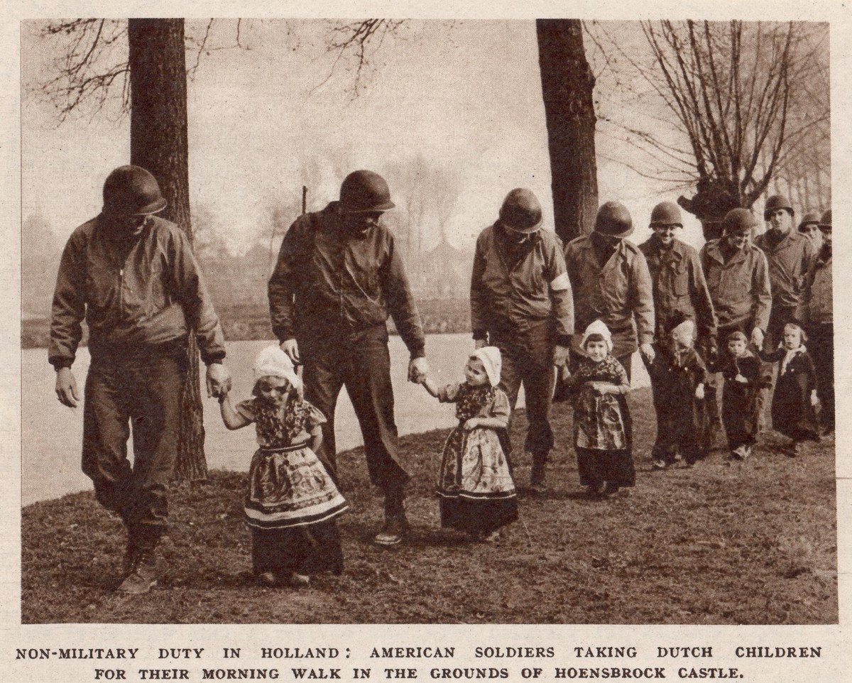 Photograph of a group of American soldiers and local children in Volendam-style costume. The photograph was taken in Hoensbroek, Limburg, The Netherlands, in 1945 or 1946 (TRC 2019.1424).