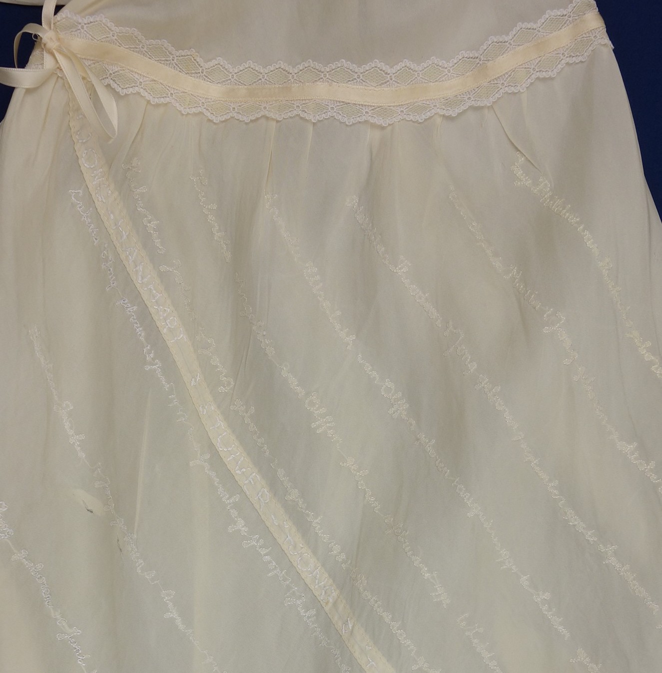 Detail of the christening gown, with the names of the baptised children embroidered in diagonal lines.