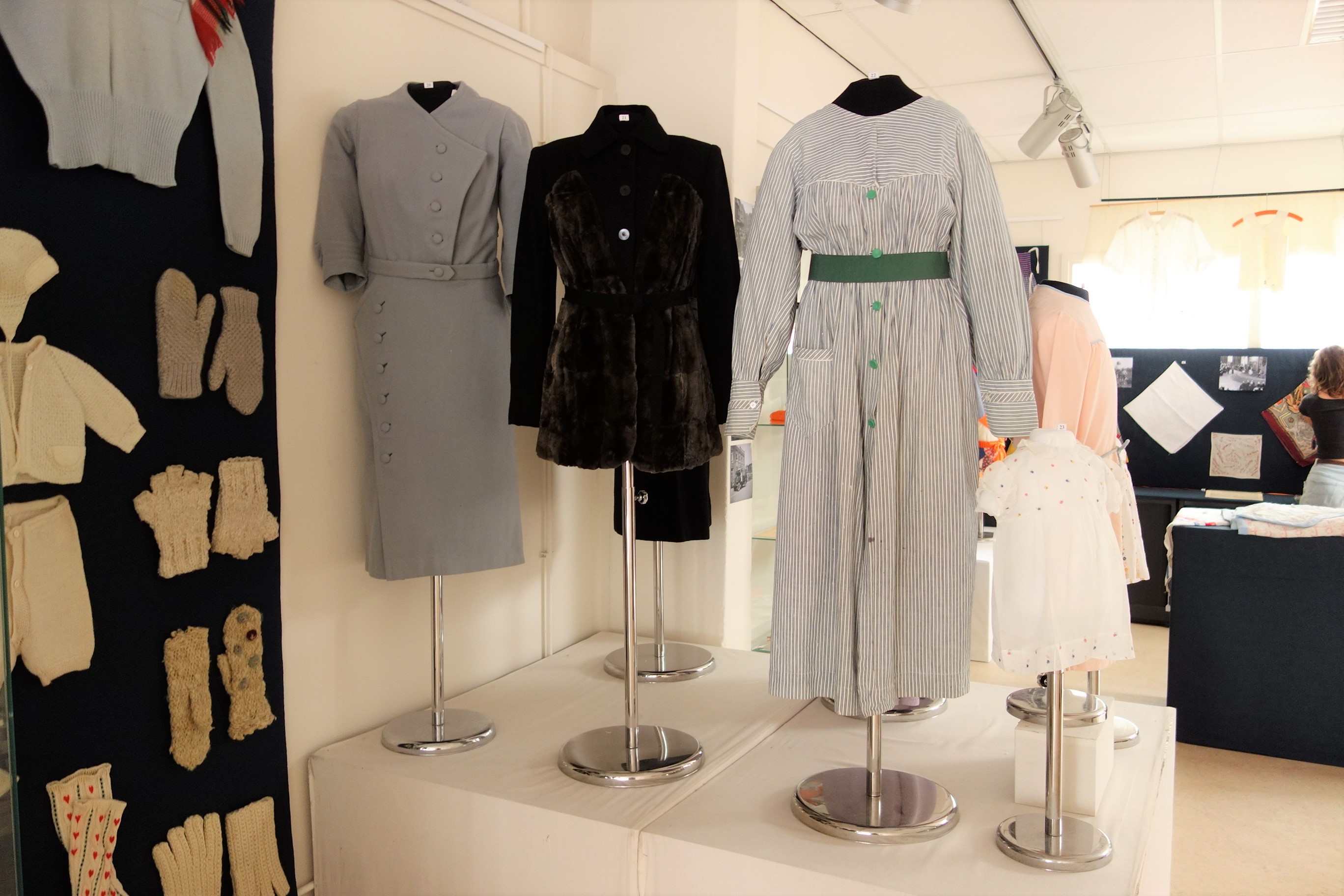 Two dresses, to the left and right, made from an old blanket and mattress ticking respectively, and in the centre a jacket decorated with mouse fur.